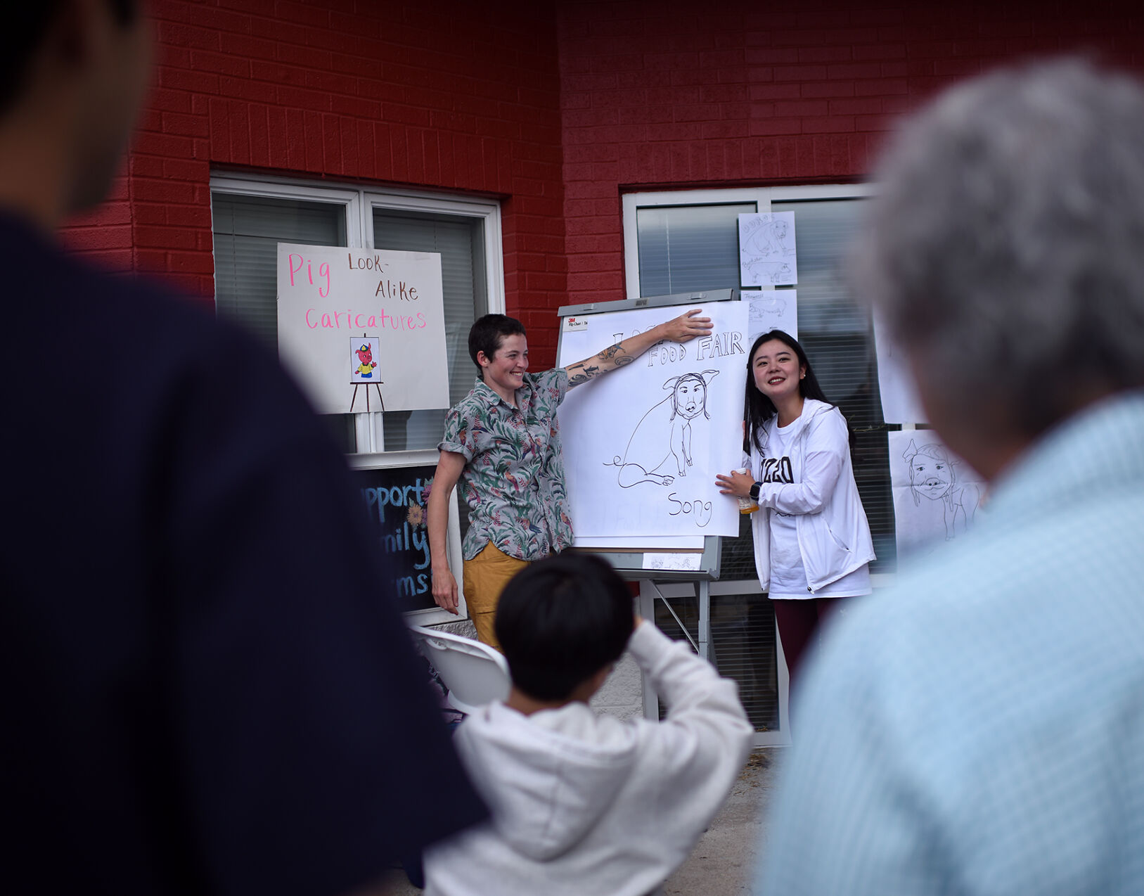 Junhyeong Jeong takes a photo of pig caricature artist Emily Lessner, left, and Song Jo on Thursday at the Missouri Rural Crisis Center in Columbia